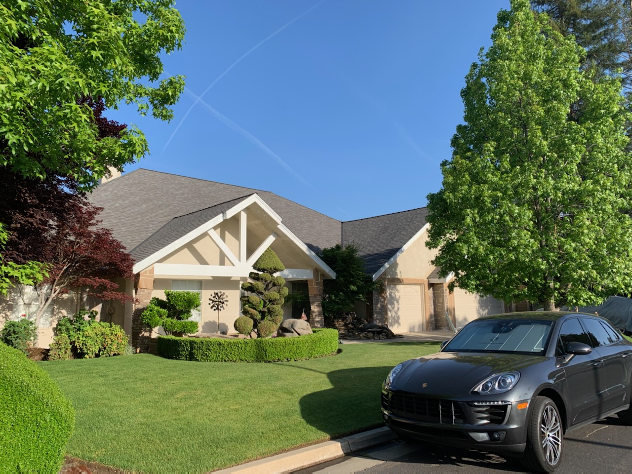 Beige house with white gable trim, a gray roof, and a green front lawn
