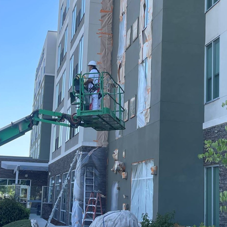 Painter on a boom lift coating a masked commercial building