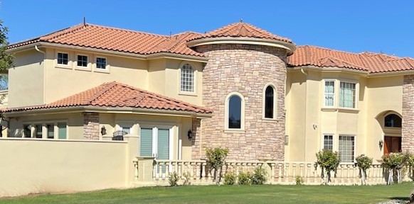 Beige stucco house with a stone turret and a tile roof under a clear sky