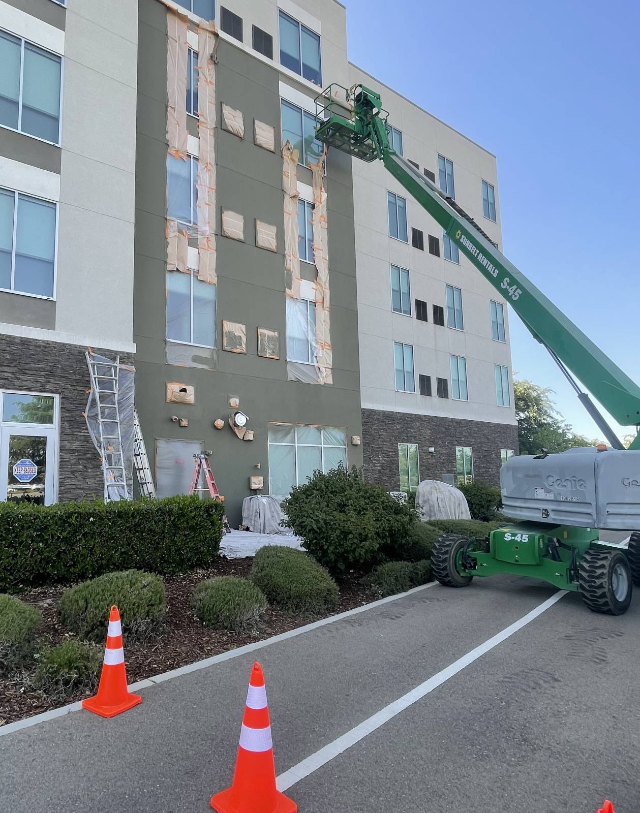Multi-story commercial building being painted, windows masked, boom lift at the facade