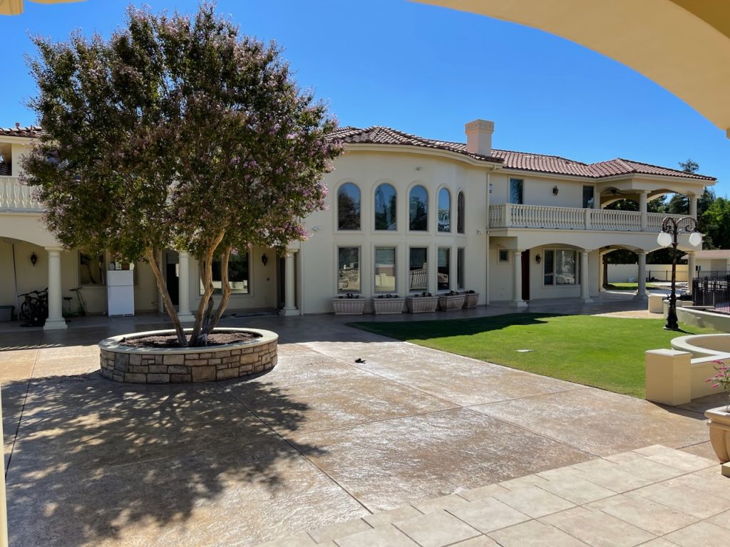 Cream stucco home with arched windows, a balcony, and a tiled roof in full sun