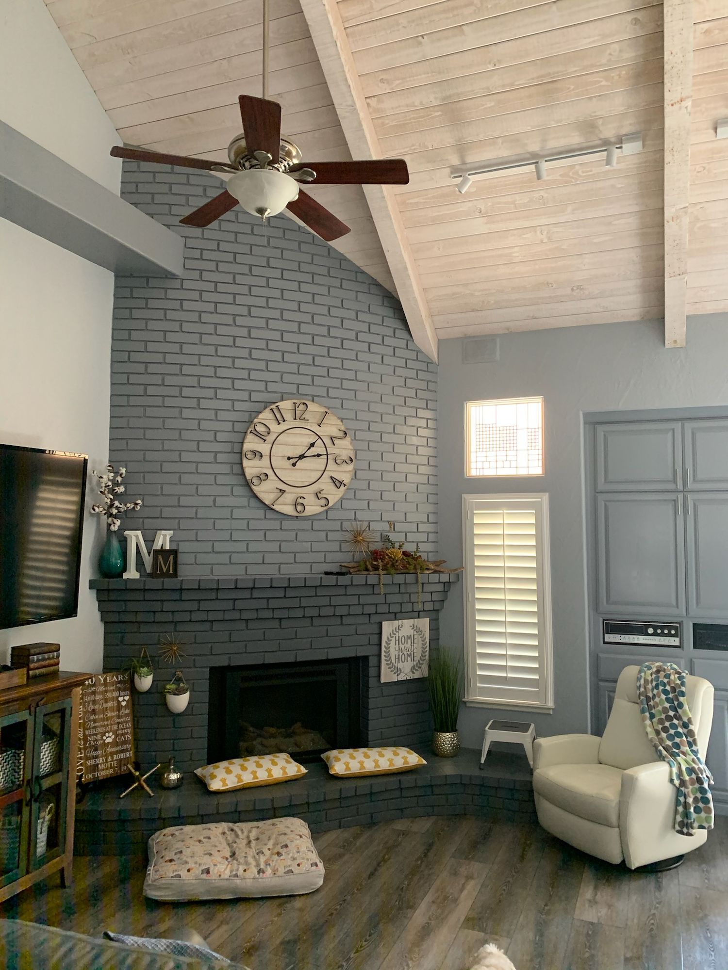 Living room with a painted gray brick fireplace, blue-gray walls, and a light wood ceiling