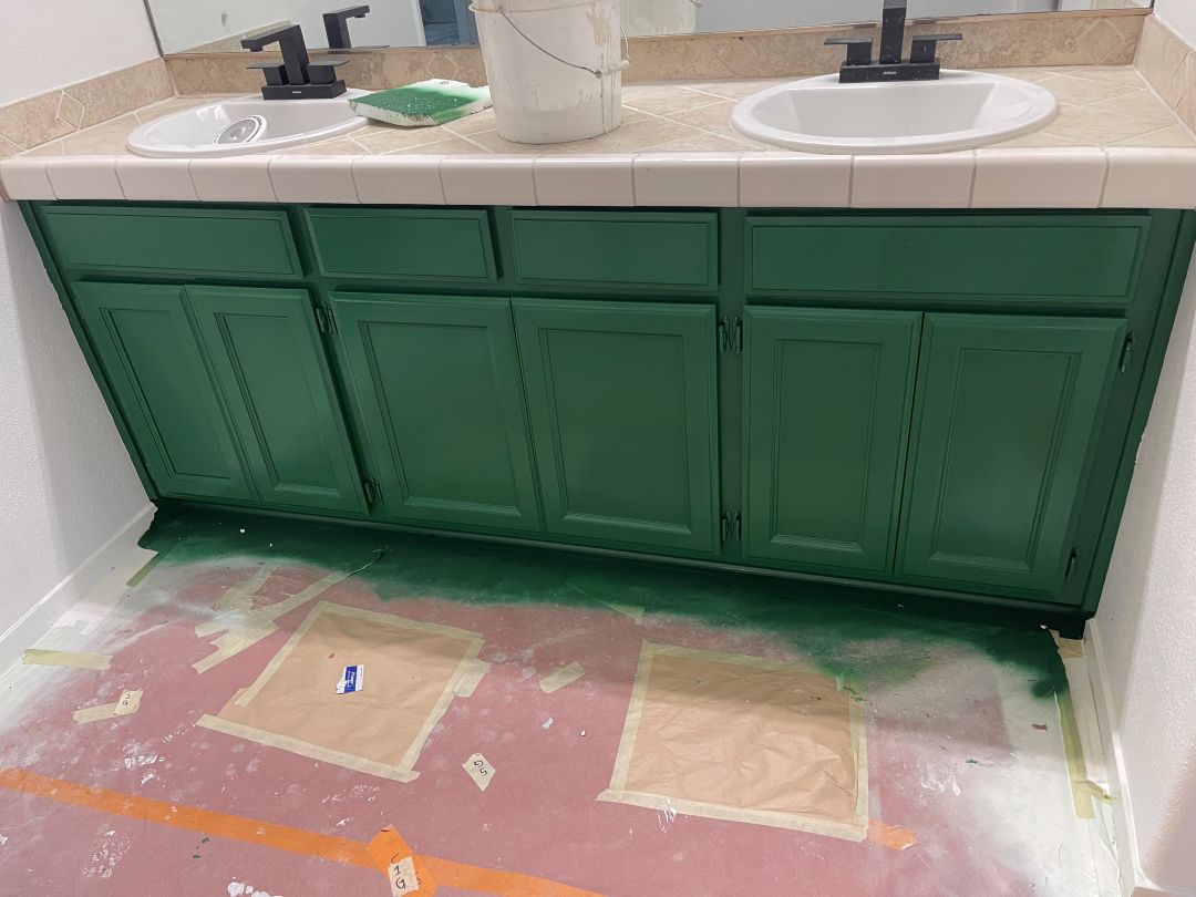Green painted kitchen cabinets with a white counter and silver hardware