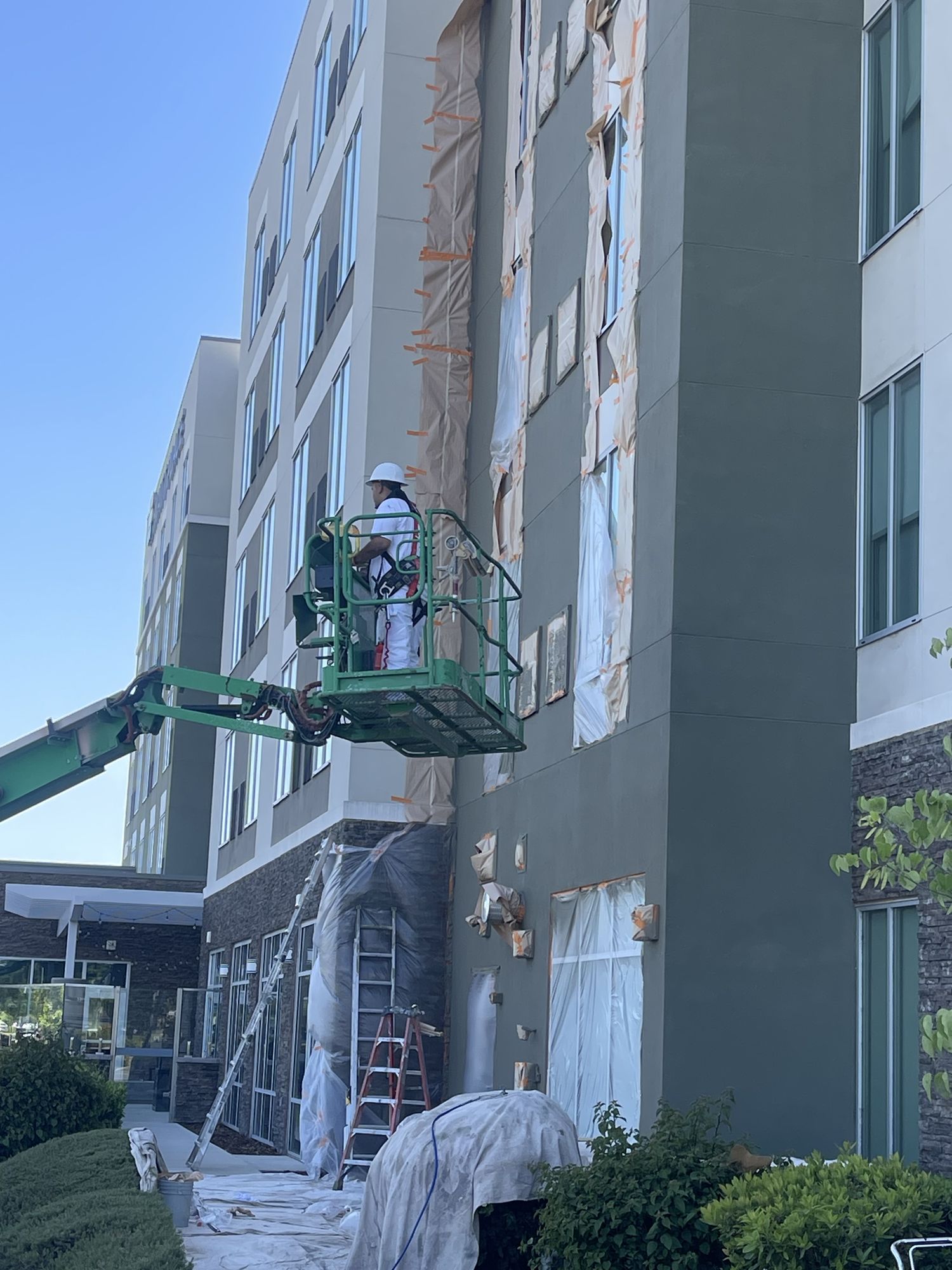Painter on a lift coating a multi-story hotel exterior, windows masked