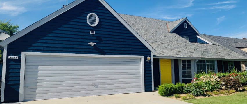 Navy house with a yellow front door, white garage, and fresh landscaping