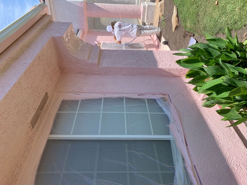 Pink stucco house in progress, with the upper wall painted and the lower wall still beige