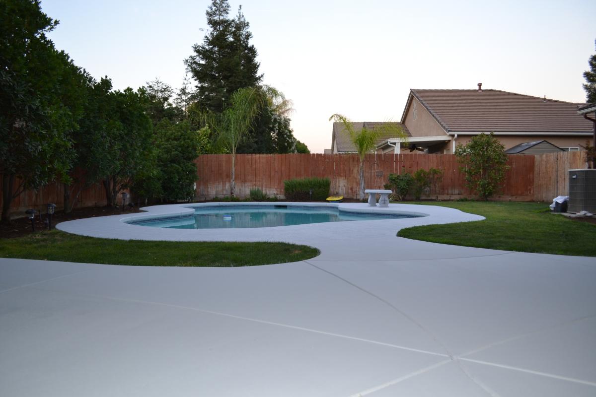 Coated gray pool deck with the pool and backyard behind it