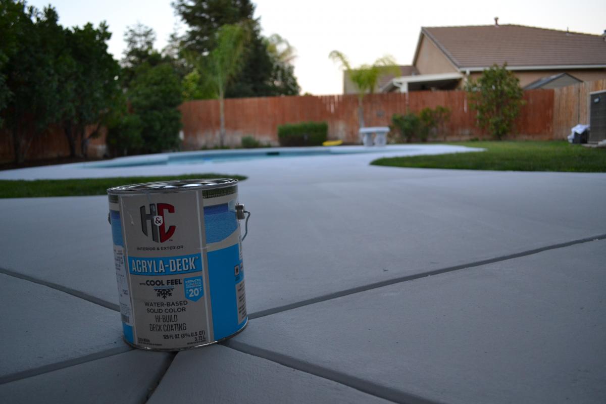 Gray coated concrete pool deck with a can of deck coating in the foreground and a backyard pool beyond
