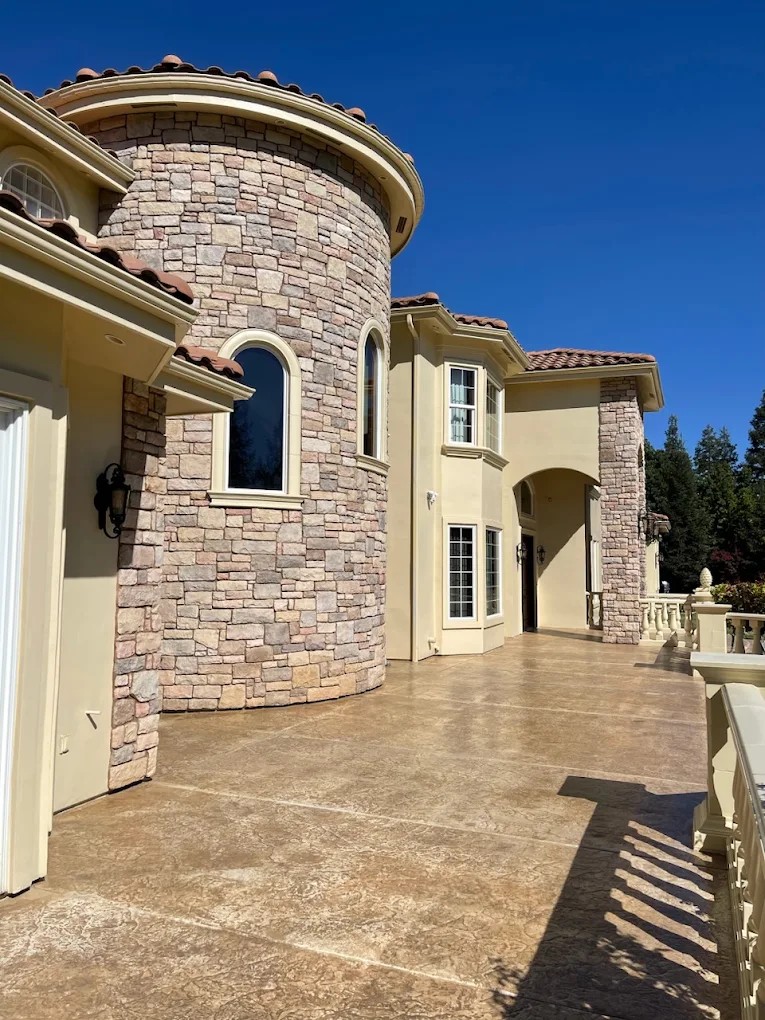 Beige stucco home with a round stone turret and a stained concrete patio
