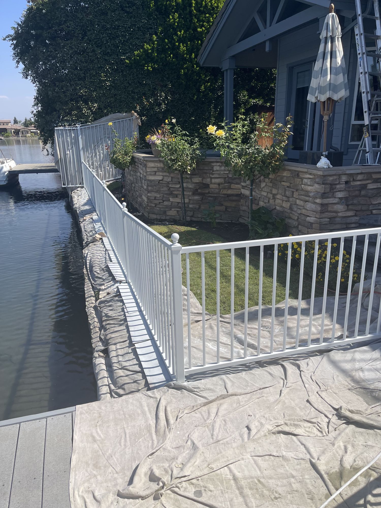 Freshly painted white metal railing along a waterfront yard, drop cloths still down